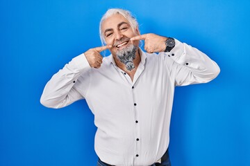 Middle age man with grey hair standing over blue background smiling cheerful showing and pointing with fingers teeth and mouth. dental health concept.