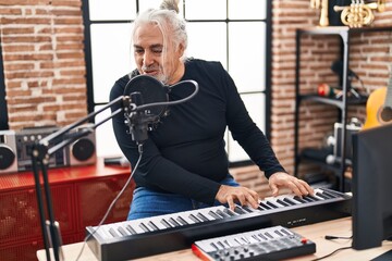 Middle age grey-haired man musician singing song playing piano at music studio