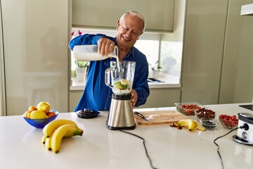Senior man smiling confident pouring milk on blender at kitchen