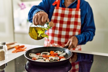 Senior man pouring oil on frying pan at kitchen