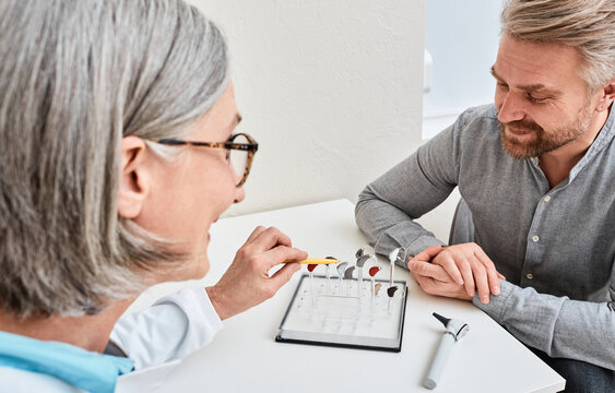 Female Audiologist Offers BTE Hearing Aids To Man Patient With Hearing Problems For Treatment His Deafness. Hearing Aid Selection