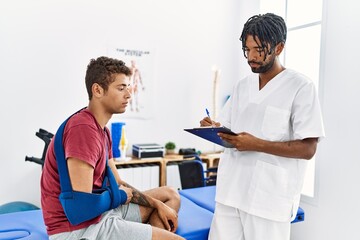 Two men physiptherapist and patient having rehab session writing accident report at clinic