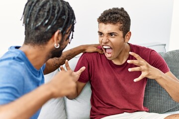 Two men fighting and screaming sitting on sofa at home
