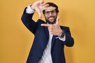Handsome latin man standing over yellow background smiling making frame with hands and fingers with happy face. creativity and photography concept.