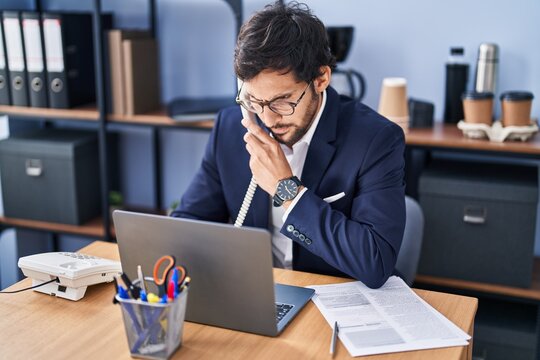 Young hispanic man business worker talking on the telephone using laptop at office