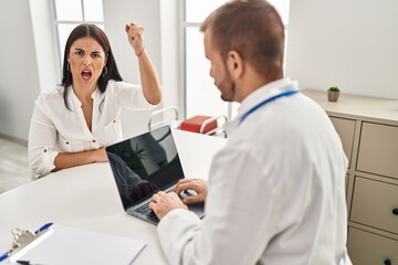 Fototapeta premium Young hispanic woman at the doctor annoyed and frustrated shouting with anger, yelling crazy with anger and hand raised