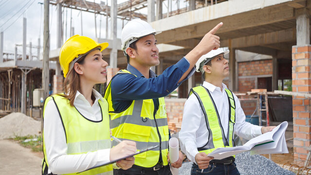 Asian Architector and engineers team with draft plan of building  talking on constructing site. Construction manager and engineer working on building site.