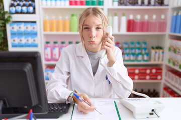 Young caucasian woman working at pharmacy drugstore speaking on the telephone depressed and worry for distress, crying angry and afraid. sad expression.