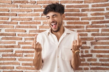 Arab man with beard standing over bricks wall background showing middle finger doing fuck you bad...
