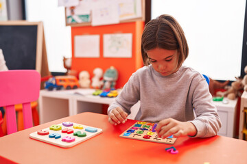 Fototapeta premium Adorable hispanic boy playing with maths puzzle game sitting on table at kindergarten