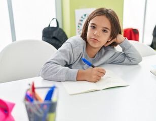 Adorable hispanic boy student writing on notebook at classroom