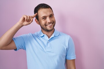 Hispanic man standing over pink background smiling pointing to head with one finger, great idea or thought, good memory