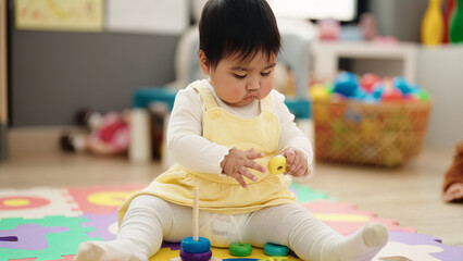 Adorable hispanic baby playing with hoops sitting on floor at kindergarten