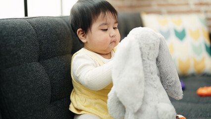 Adorable hispanic baby holding toy sitting on sofa at home