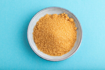 plate with unrefined golden cane sugar on blue pastel. top view, close up.