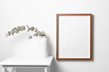 Portraut picture frame mockup on white wall with dry eucalyptus twig decoration in minimalistic...