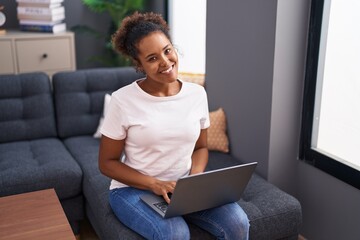 African american woman using laptop sitting on sofa at home