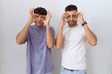 Homosexual gay couple standing over white background trying to open eyes with fingers, sleepy and tired for morning fatigue