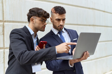 Two hispanic men business workers using laptop and smartphone over isolated white background