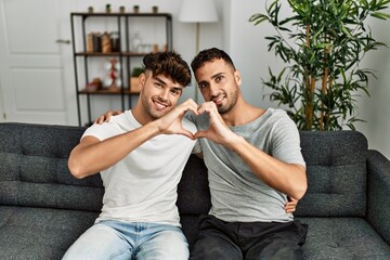Two hispanic men couple smiling confident doing heart shape with hands at home