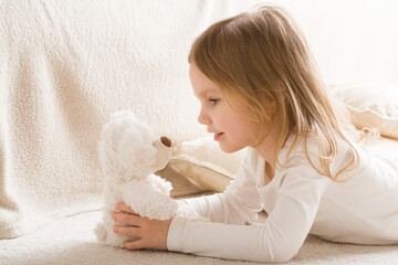 Adorable smiling little girl playing with white soft teddy bear on carpet at nursery room. Hands...
