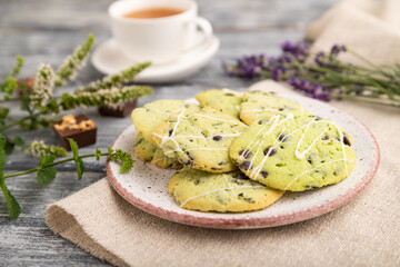Green cookies with chocolate and mint with cup of green tea on gray wooden background. side view, close up, selective focus.