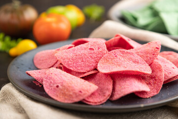 Green and red potato chips with herbs and tomatoes on black concrete background. Side view, close up, selective focus.