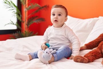 Adorable caucasian baby playing with toys sitting on bed at bedroom