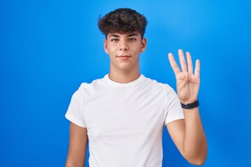 Hispanic teenager standing over blue background showing and pointing up with fingers number four...