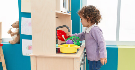 Adorable hispanic girl playing with play kitchen standing at kindergarten