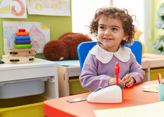 Adorable hispanic girl playing with toy sitting on table at kindergarten