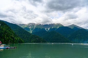 Alpine Lake Ritsa. Tourists on catamaran sailing along lake among mountains.
