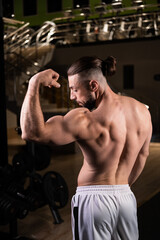 Fototapeta na wymiar A handsome bearded male athlete with a muscular body poses and shows biceps in the gym