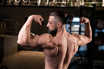 Fototapeta na wymiar A handsome bearded male athlete with a muscular body poses and shows his biceps and back in the gym
