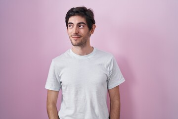 Young hispanic man standing over pink background smiling looking to the side and staring away thinking.