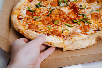 Close-up hand taking slice of fresh pizza with tomato sauce, mozzarella, spicy chorizo, bell peppers, selective focus