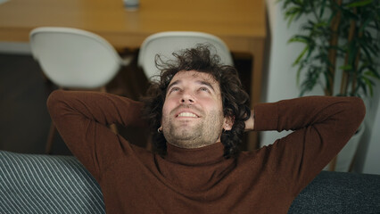 Young hispanic man relaxed with hands on head sitting on sofa at home