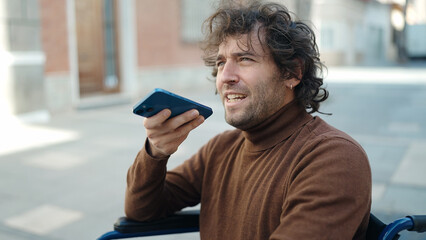 Young hispanic man talking on smartphone sitting on wheelchair at street
