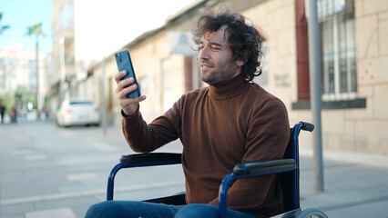 Young hispanic man using smartphone sitting on wheelchair at street