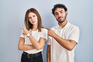 Young couple wearing casual clothes standing together pointing with hand finger to the side showing advertisement, serious and calm face