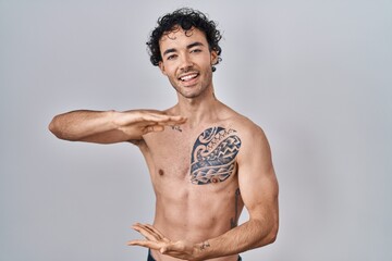 Fototapeta premium Hispanic man standing shirtless gesturing with hands showing big and large size sign, measure symbol. smiling looking at the camera. measuring concept.