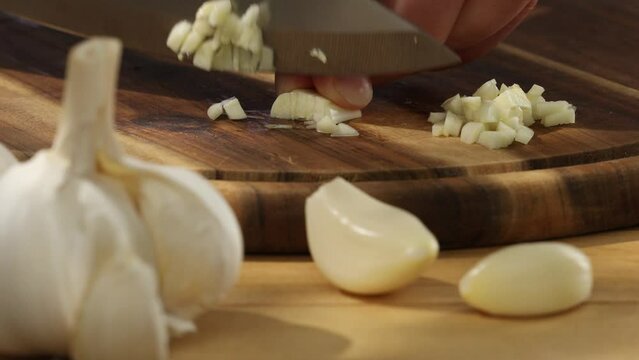  garlic on a wooden chopping board close-up. a knife grinds a clove of garlic surrounded by whole ones. kitchen on a sunny day. High quality photo