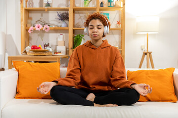 Yoga mindfulness meditation. Young healthy african girl practicing yoga at home. Woman sitting in lotus pose on yoga mat meditating smiling relaxing indoor. Girl doing breathing practice, yoga at home