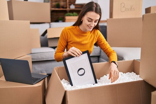 Young caucasian woman smiling confident unpacking cardboard box at new home
