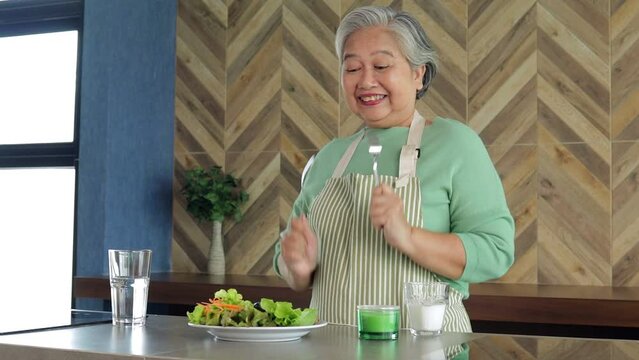 Asian healthy senior woman cooking simple food in kitchen at home in morning time. Cheerful smile happy eating healthy food. Nutritious food for the elderly