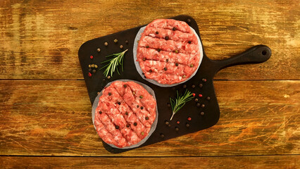 Raw meat burger cutlets, with spices and rosemary sprigs on kitchen board. Tasty cutlets preparation on domestic kitchen. - 568838470