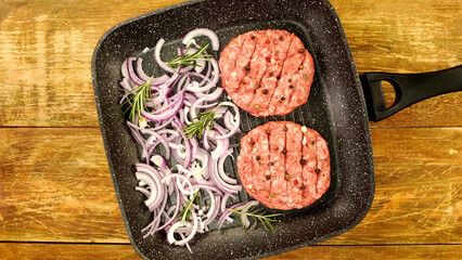 Raw meat burger cutlets, with spices, sliced onion and rosemary sprigs on frying pan. - 568838487