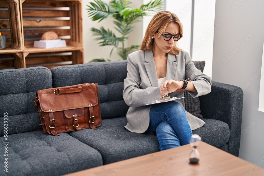 Poster Hispanic woman working at consultation office checking the time on wrist watch, relaxed and confident