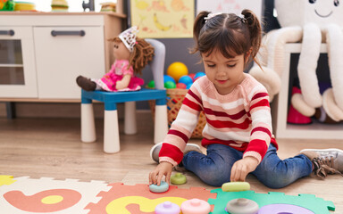 Adorable hispanic girl playing with toys sitting on floor at kindergarten