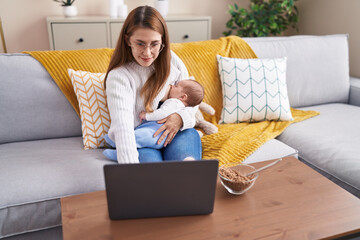 Mother and son using laptop breastfeeding baby at home
